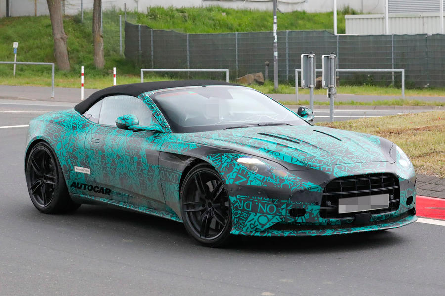 Camouflaged Aston Martin DB12 Volante driving around roundabout, front end