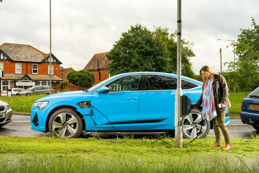 Audi E-tron azul brilhante sendo conectado ao carregador de carro elétrico do poste de luz