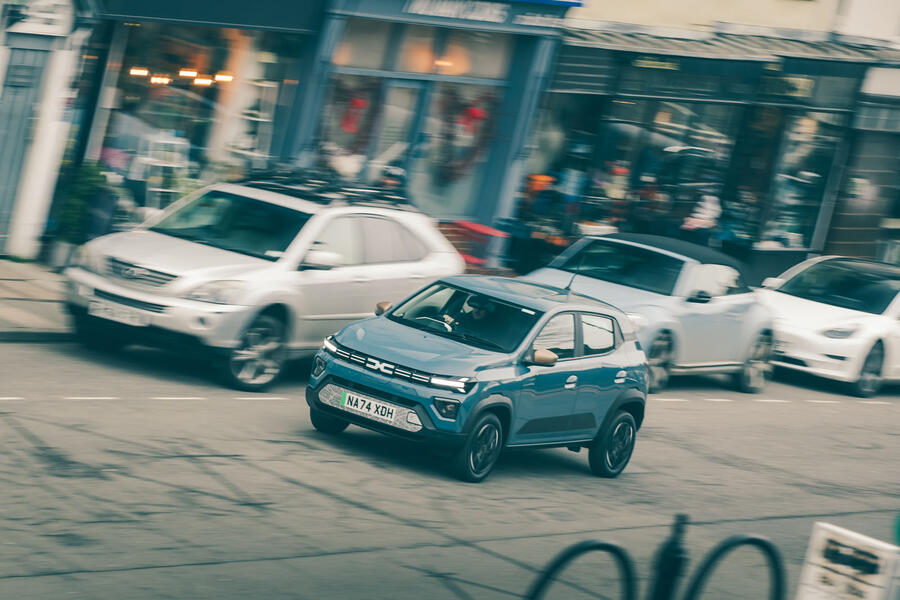 Dacia Spring driving through town, viewed from the front-left quarter