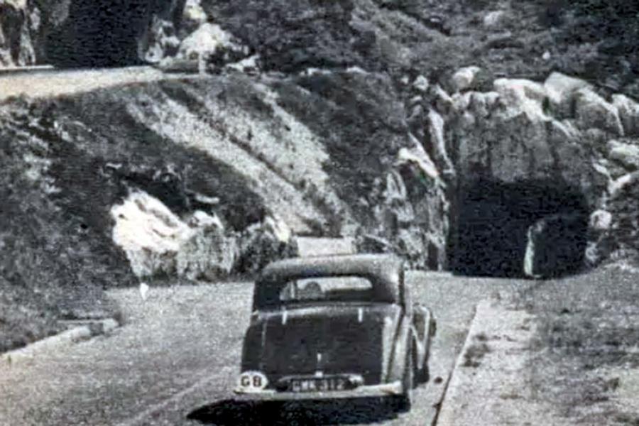 Old car with 'GB' identification plate driving into rocky tunnel