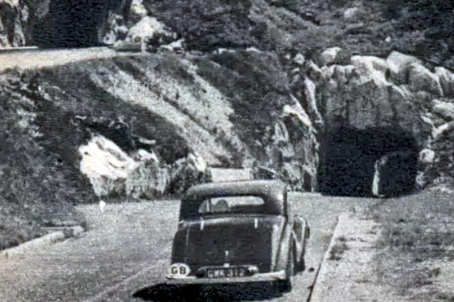 Carro antigo com placa de identificação 'GB' entrando em túnel rochoso