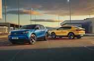 A blue Ford Capri parked next to a yellow Ford Capri in an industrial setting at sunset